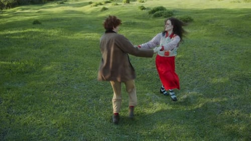 Young Carefree Couple Holding Hands and Spinning in Green Meadow