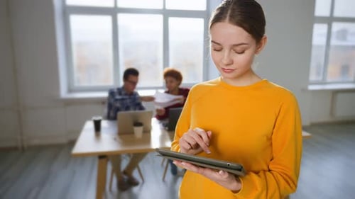 Portrait of Young Beautiful Caucasian Woman Stands in Office at Workplace with Digital Tablet
