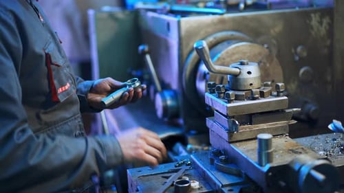 Turner in the uniform standing at his workplace. Man holding a metal detail and examining it.