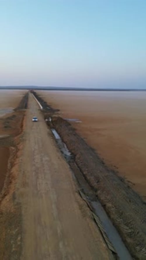 Une vue aérienne montre une voiture roulant sur une route droite à Kutch avec des dunes dorées des deux côtés