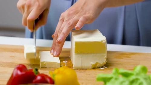 Jeune femme découpant du fromage feta sur une planche de bois à la maison préparant des aliments sains
