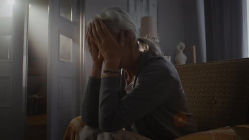 Elderly Woman Drops Head Onto Palms of Frustration at Home