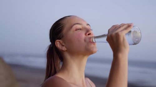 Woman Drinking Water From Glass Bottle After Sport Training Jogging or Yoga Practice Near Ocean