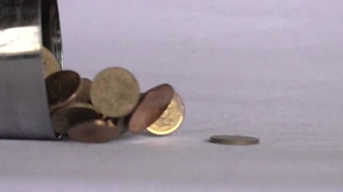 A slow motion video of coins pouring out of a metal jar.