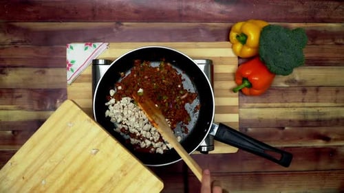 A Top view of adding chicken into the ingredients in pan, placed on a stove, two big yellow and red