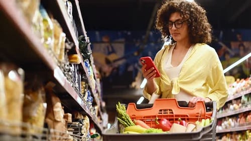 By the shelves with products. Gorgeous woman is in the grocery store.