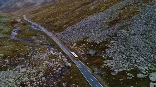Yellow Bus Driving Through A Rugged And Rocky Mountain Pass
