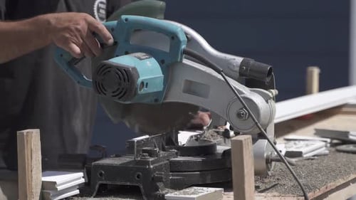 Close up of labourer cutting piece of wood with electric circular saw in slow motion.