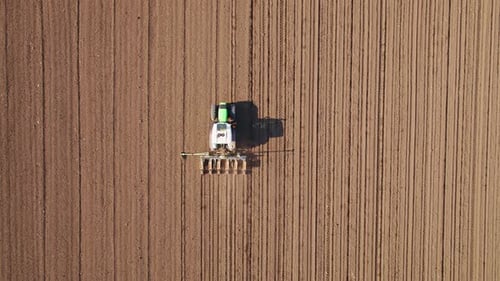 Aerial drone shot of a farmer in tractor seeding, sowing agricultural crops at field.