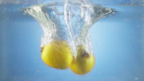 Two Yellow Fruits Dropping into Clear Water