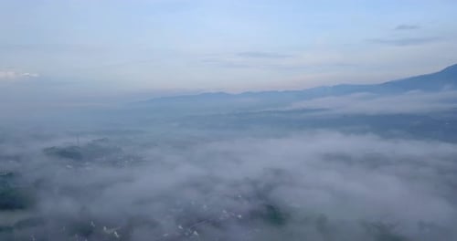 Drone footage flyover sea of fog above urban areas - Tropical city in Indonesia