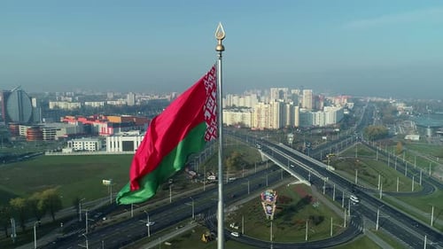 Bandeira da Bielorrússia balançando sobre o céu azul e a paisagem urbana de Minsk em uma manhã ensolarada