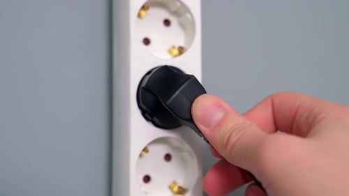 Hand Plugging Black Electrical Plug into Outlet