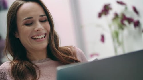 Woman smiles while using laptop in bright apartment