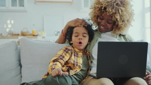 Happy Mother and Little Son Watching Cartoon on Laptop on Couch at Home