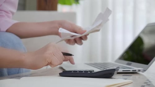 Person Calculating Finances Using Calculator and Laptop