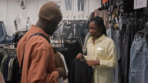 Black Man Choosing Clothes in Shop with Help of Sales Assistant