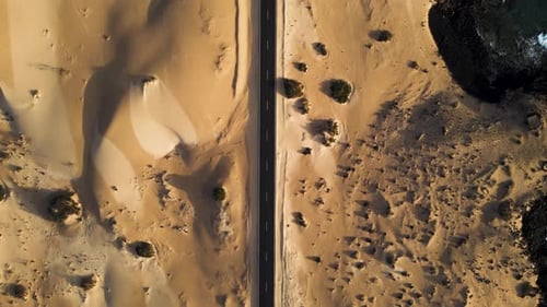 Aerial view of sandy dunes and winding road by ocean, Spain.