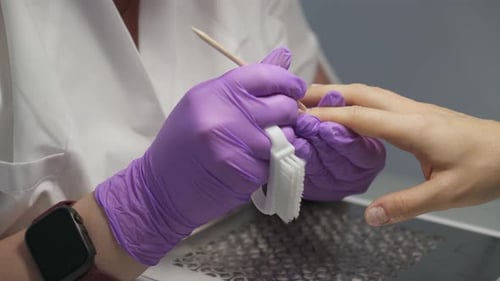 Nagelhautpflege bei professioneller Maniküre mit lila Handschuhen