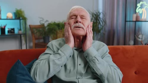 Senior Man Massaging Temples With Headache Indoors