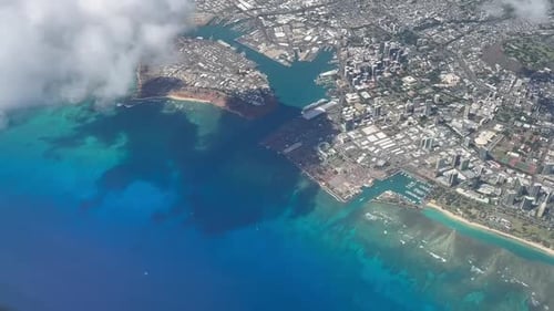 Airplane view flying over Honolulu's busy downtown skyline overlooking the crystal clear blue waters