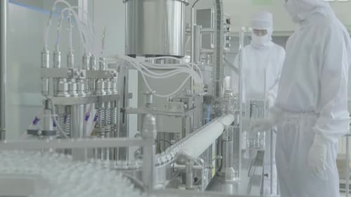 Ligne de production dans un environnement stérile avec des ouvriers de laboratoire en gants de lavage en arrière-plan.