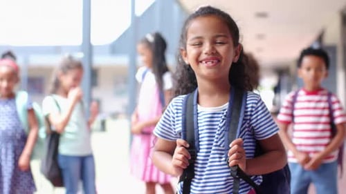 Smiling girl with backpack standing in school hallway with friends in background