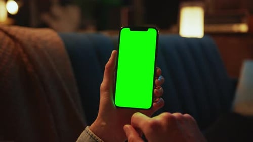 Indoors Hands Man Holding and Using a Mobile Phone with a Vertical Green Screen Lying on a Sofa