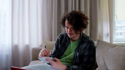 Young Man Writing in Notebook on Couch