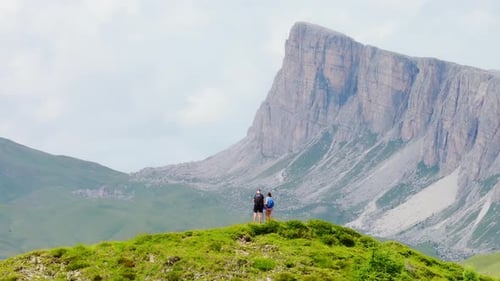 Couple admires towering mountain cliff from scenic green hilltop in Dolomites