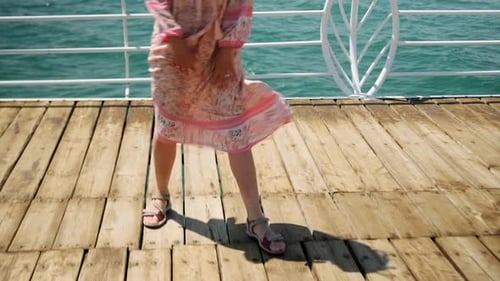 On pier beautiful dancing girl in long dress enjoying picturesque view near summer sea beach