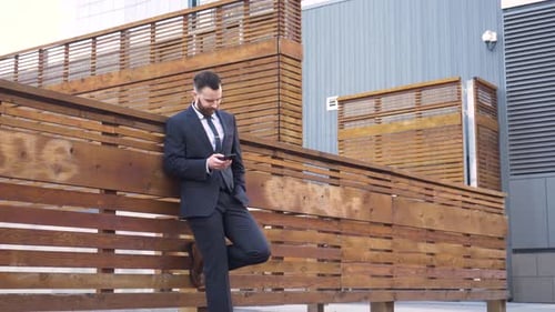 Man in Suit Using Phone Leaning on Wood