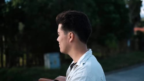 Young Male Artist Walking In The Street With An Acoustic Guitar