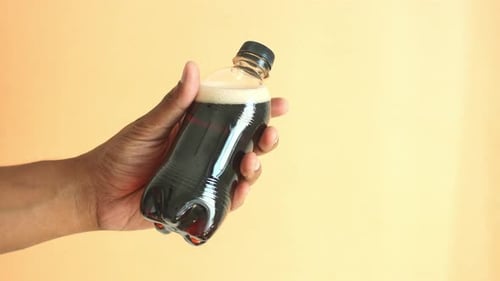 Men Holding a Plastic Bottles of Soft Drink Against Orange Background