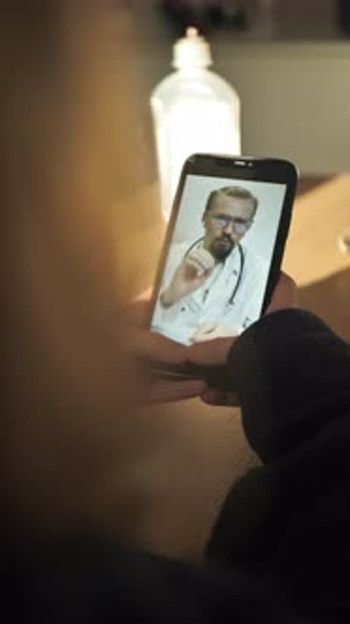 Vertikaler Blick von hinten: Mädchen mit Smartphone wird per Videoanruf vom Arzt konsultiert