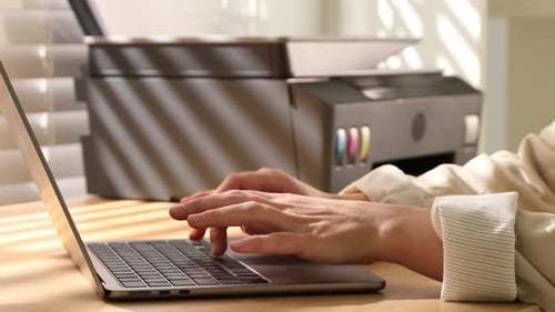 Mujer usando la impresora mientras trabaja en una computadora portátil en un escritorio de madera en el interior, primer plano