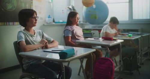 Primary School Children Sitting at the Desks Raising Hands to Give Correct Answer