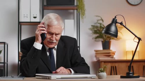 Älterer kaukasischer Geschäftsmann, Opa im Anzug, arbeitet und telefoniert am Schreibtisch zu Hause