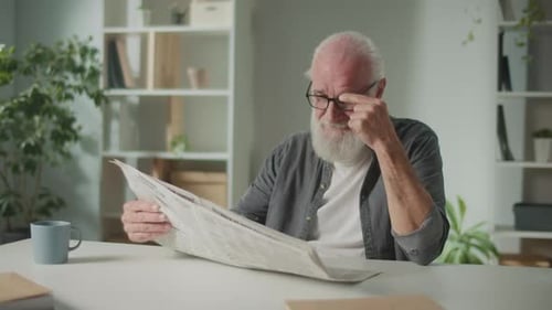 Senior Man Reading Newspaper and Smiling Indoors