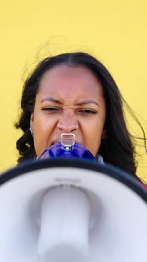 Woman Speaking into Megaphone Against Yellow Background