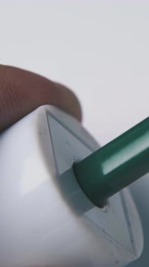 Person Puts Green Pencil Into Sharpener on Light Background