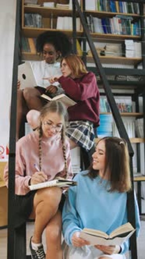 Estudantes multirraciais estudando em uma escada em uma biblioteca engajados em ler, escrever e usar um