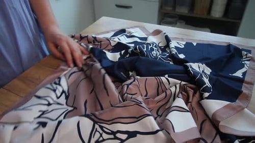 Woman Folding Patterned Scarf on Table