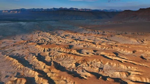 Lifeless dry uneven desert lit by the setting sun. Drone footage over the arid landscape of Utah