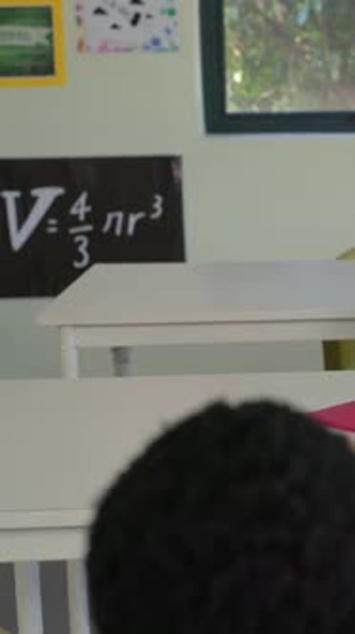 Vertical video: Panning to show kid in yellow resting while she in pink typing on laptop at school