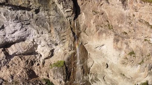 high mountain waterfall from the rocky wall with rainbow colors, aerial pullback shot