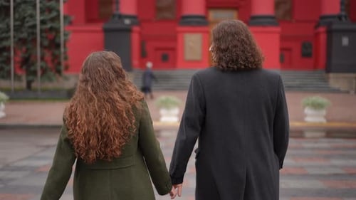 Couple with Curly Hair Walk Hand-in-Hand in City