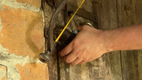 Man Cutting Through Padlock With Saw on Rustic Door