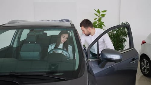 Woman Sits in Car, Man Talks in Dealership