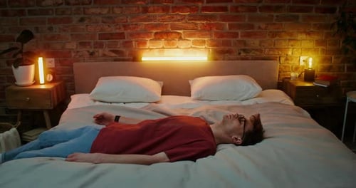 Man Falls Backwards Onto Bed in Warmly Lit Room